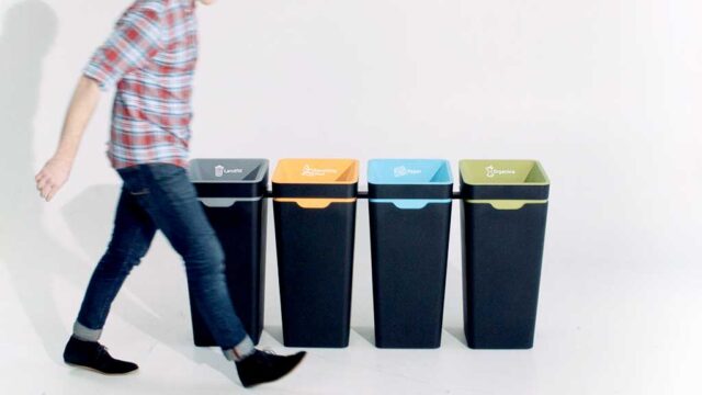 4 recycling bins of different colours, person walking past